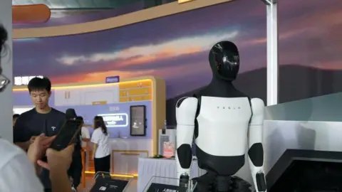 Getty Images People look at a human-like Tesla robot at a technology fair in Shanghai, China.